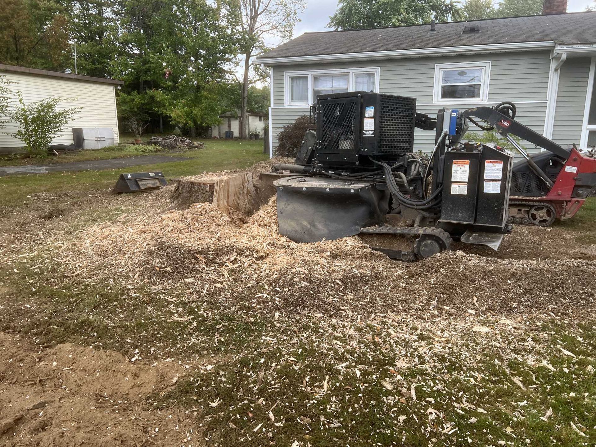 A stump grinder is sitting in the dirt in front of a house.