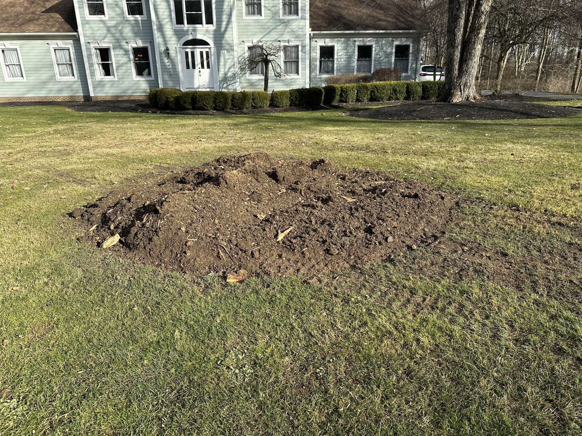 There is a pile of dirt in the grass in front of a house.