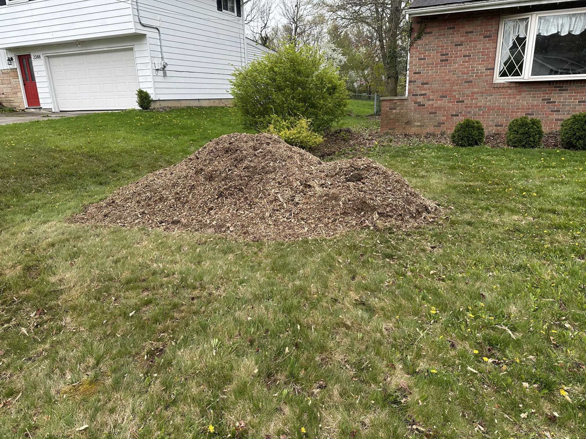 A pile of mulch is sitting in the grass in front of a house.