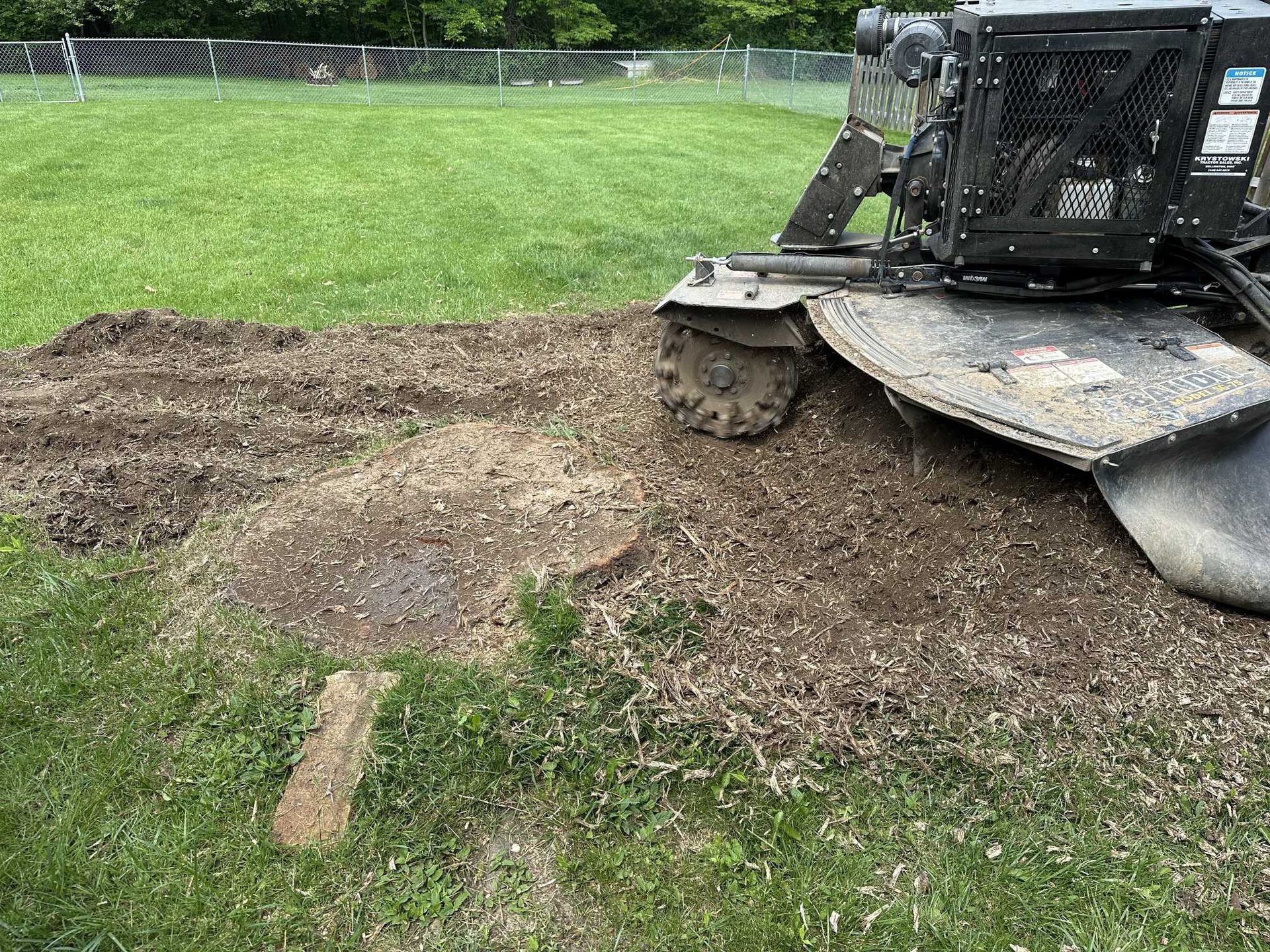 A stump grinder is cutting a tree stump in a lush green field.