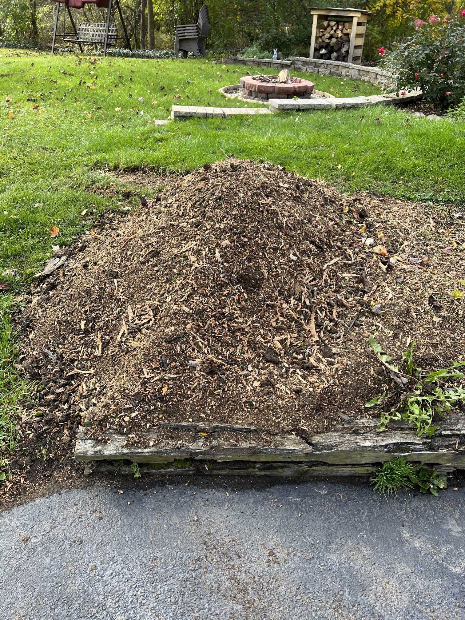 A pile of mulch is sitting on the side of a road in a yard.