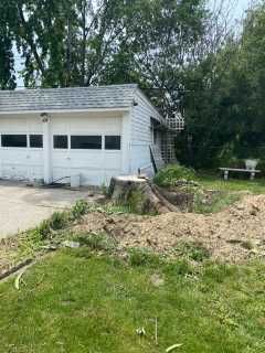 A white garage with a tree stump in front of it.