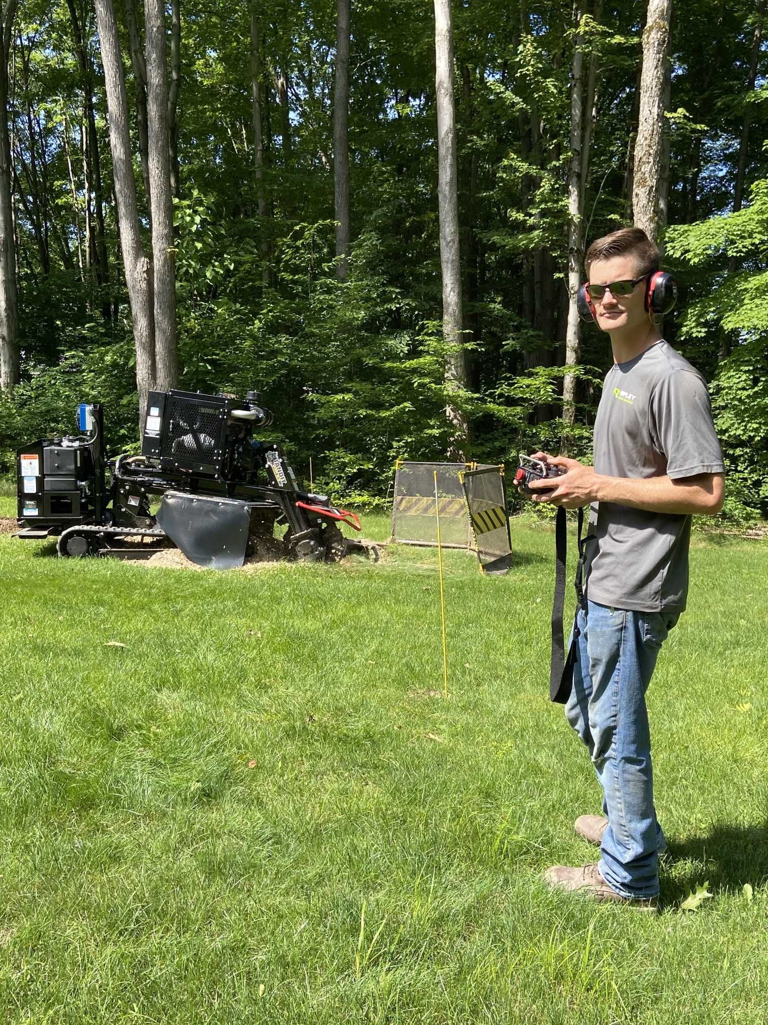 A young man is standing in a grassy field holding a remote control.