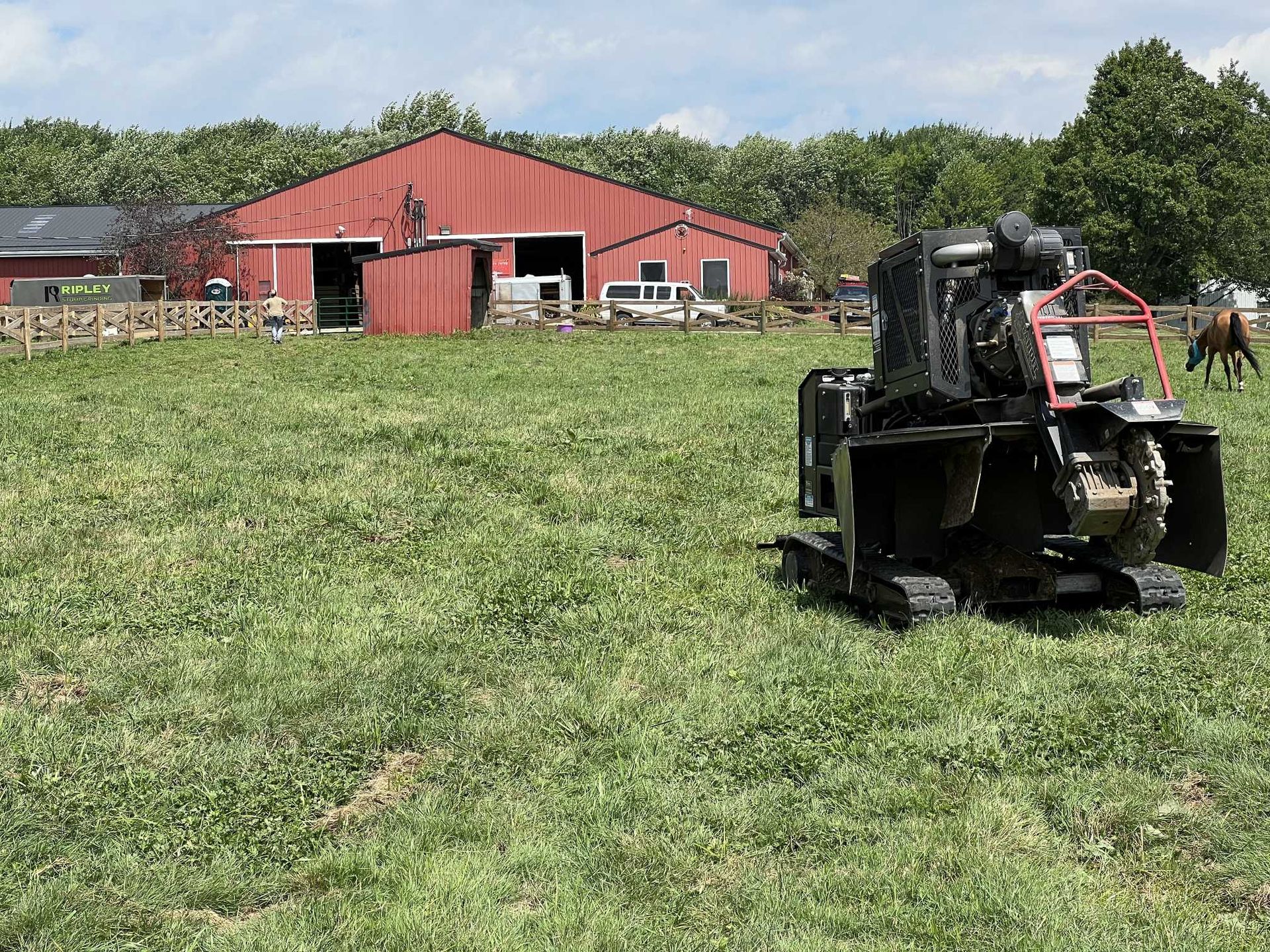 A tractor is cutting grass in a field with a horse in the background.