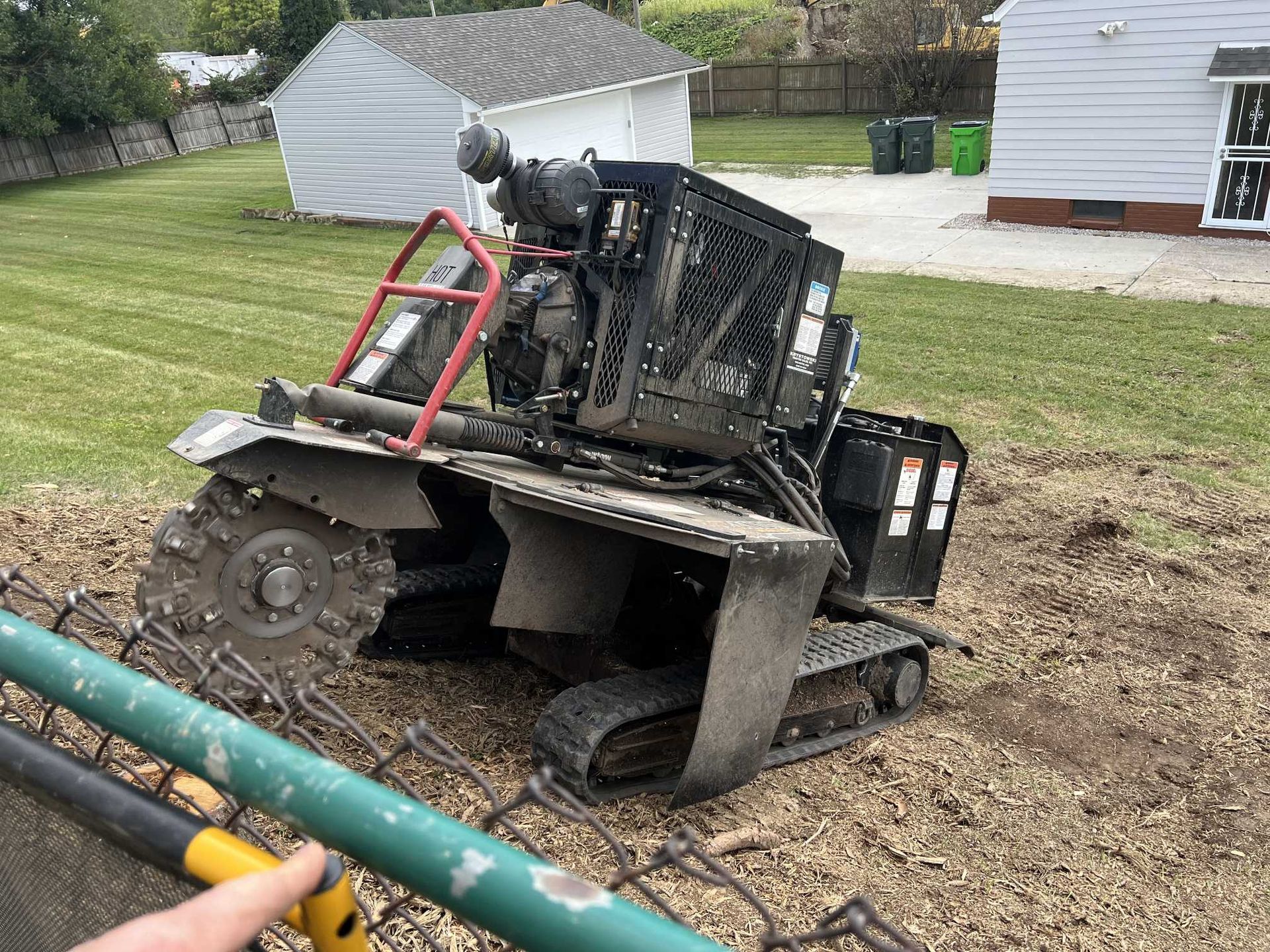 A person is pointing at a stump grinder in a yard.