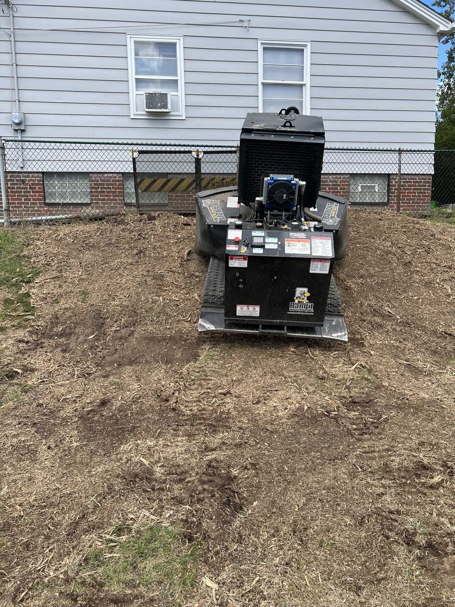 A stump grinder is sitting in the dirt in front of a house.