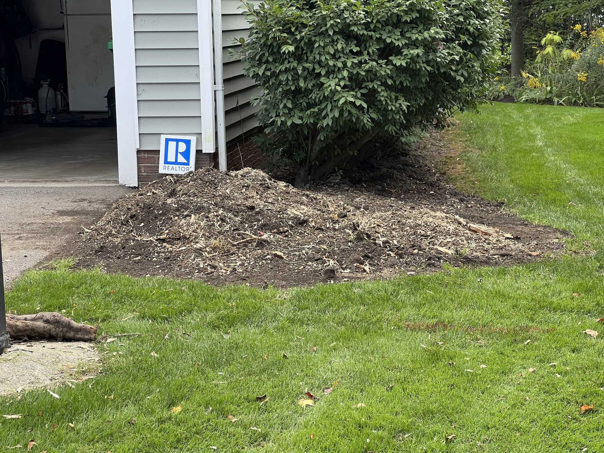 A pile of dirt is in the grass in front of a house.