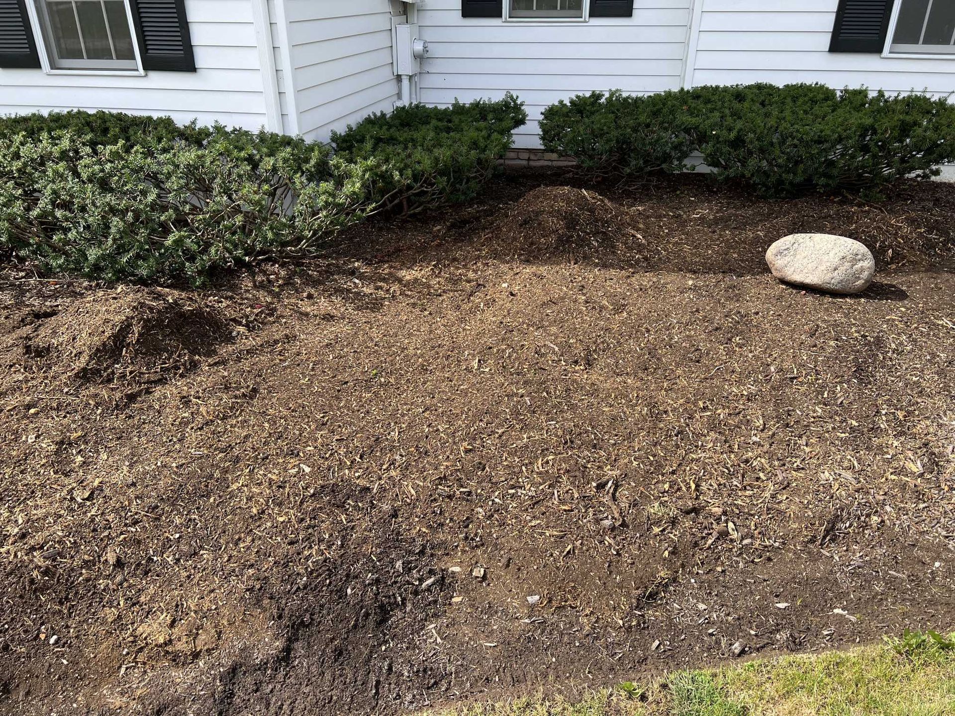 There is a large rock in the middle of the dirt in front of a house.