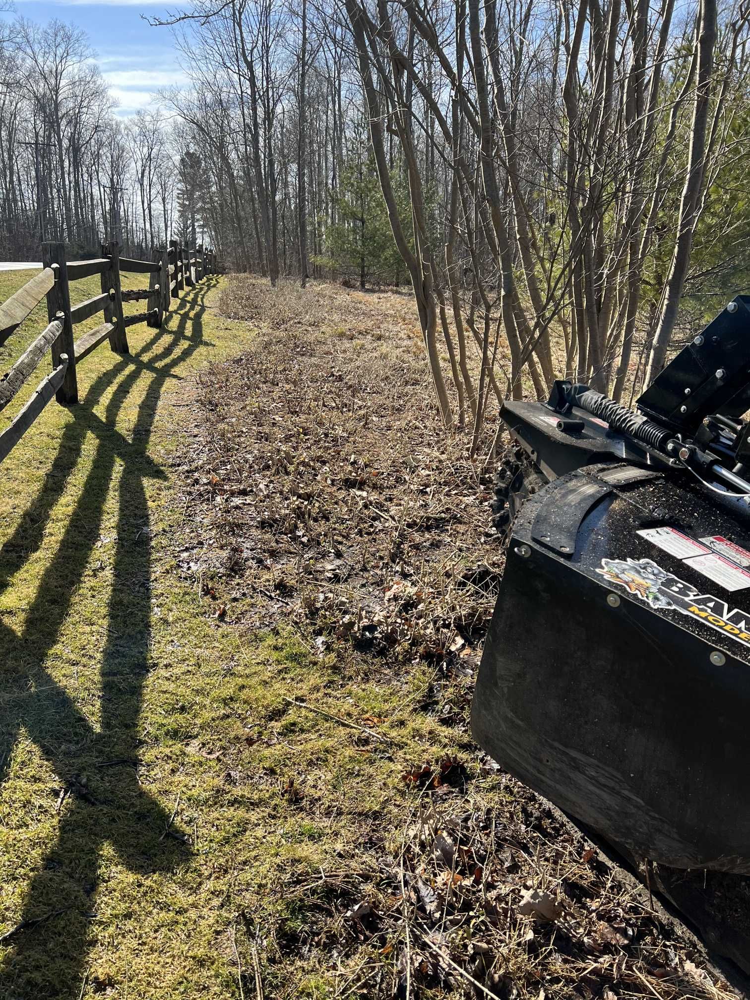 A tractor is driving down a dirt road next to a wooden fence.