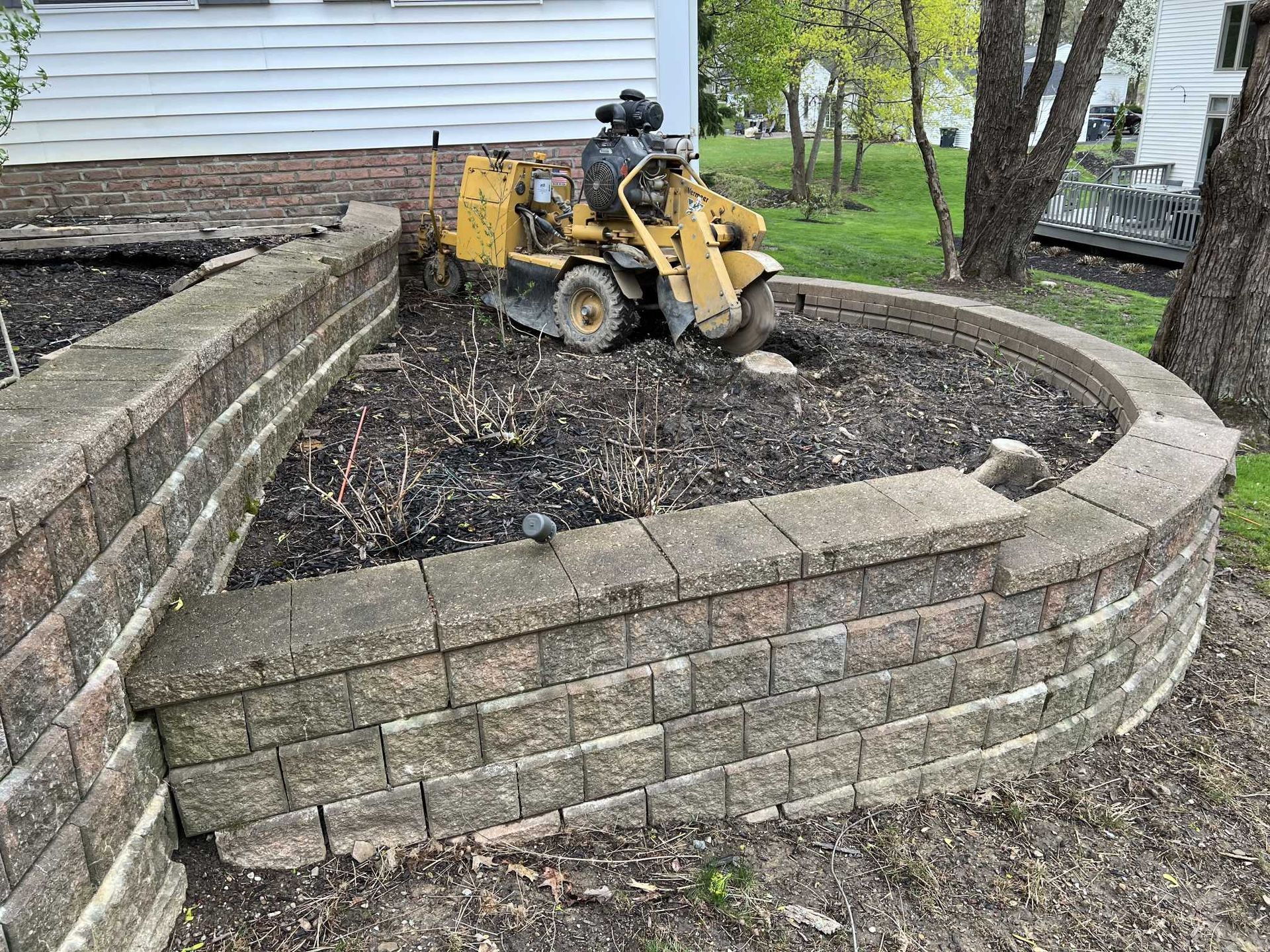 A stump grinder is sitting on top of a brick wall.
