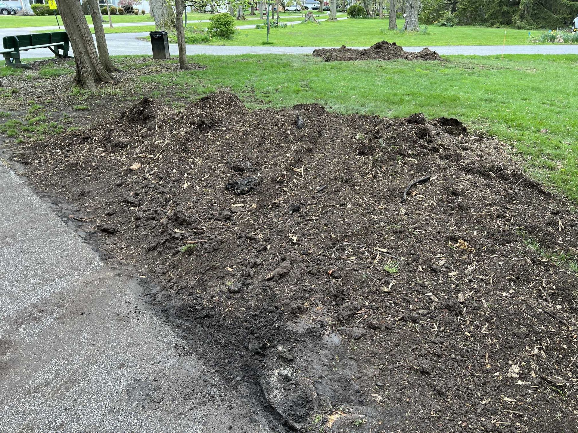 A pile of dirt is sitting on the side of a road next to a park.