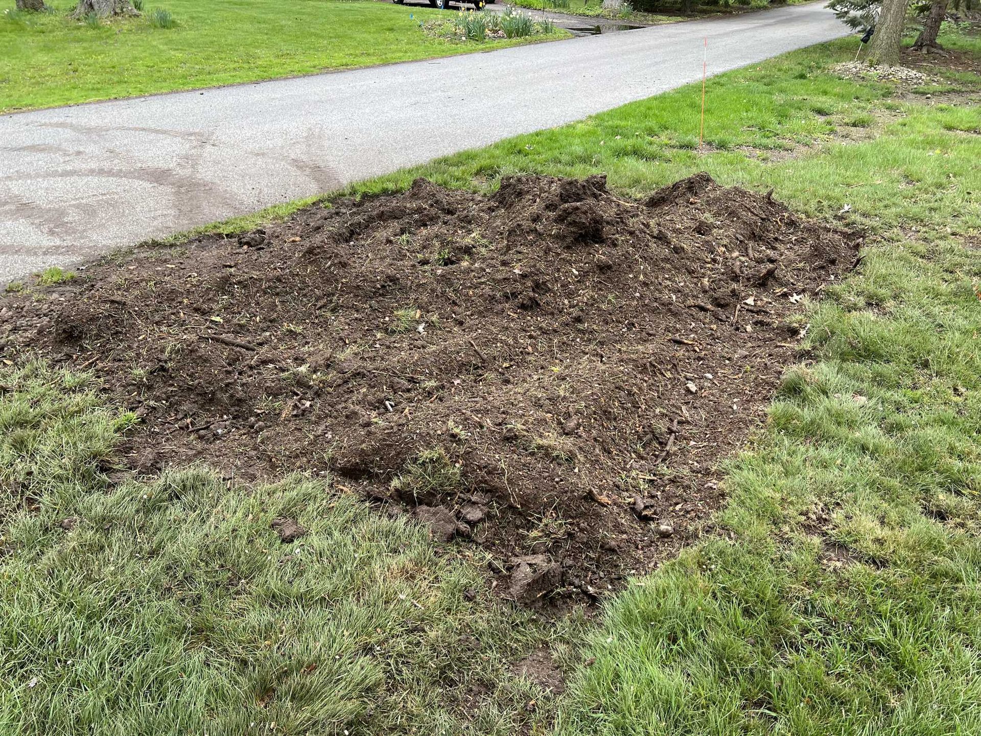 A pile of dirt is sitting in the grass next to a road.