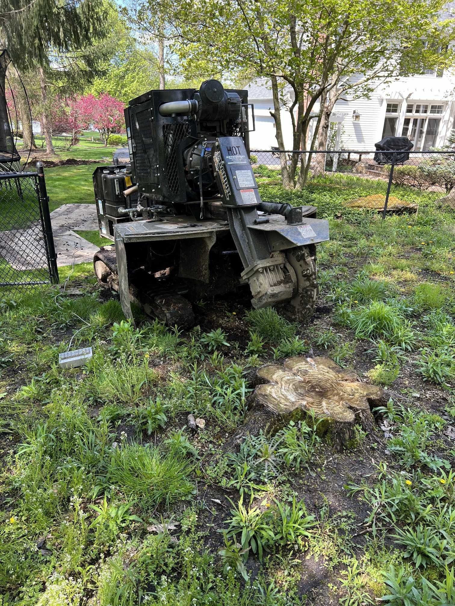 A stump grinder is sitting in the grass next to a tree stump.