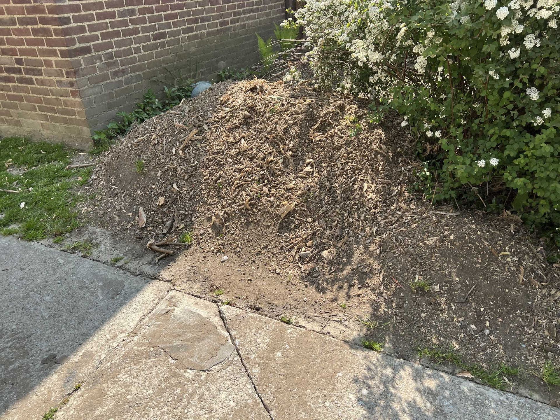 A pile of dirt is sitting on the sidewalk next to a brick building.