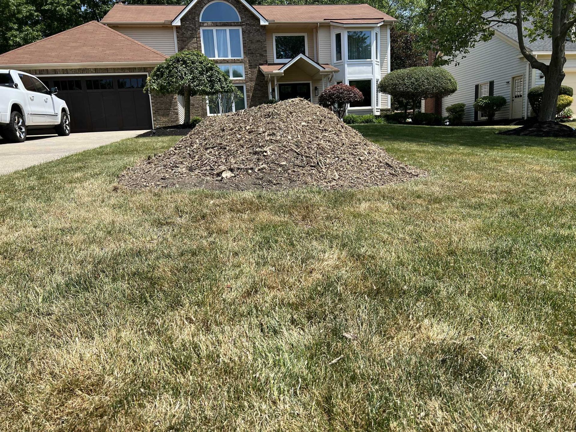 A large pile of dirt is in the middle of a lush green lawn in front of a house.