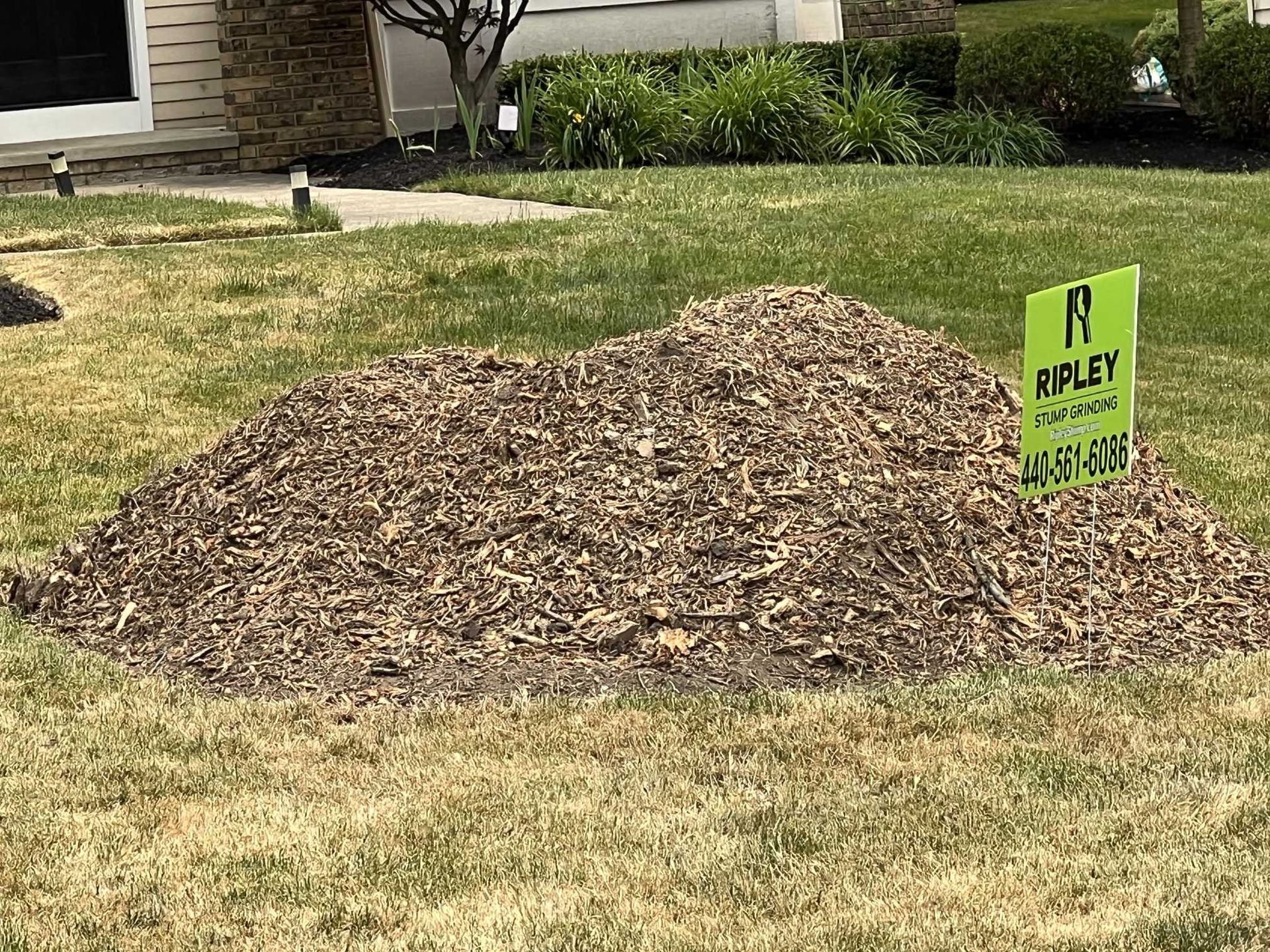 A pile of mulch is sitting in the grass in front of a house.