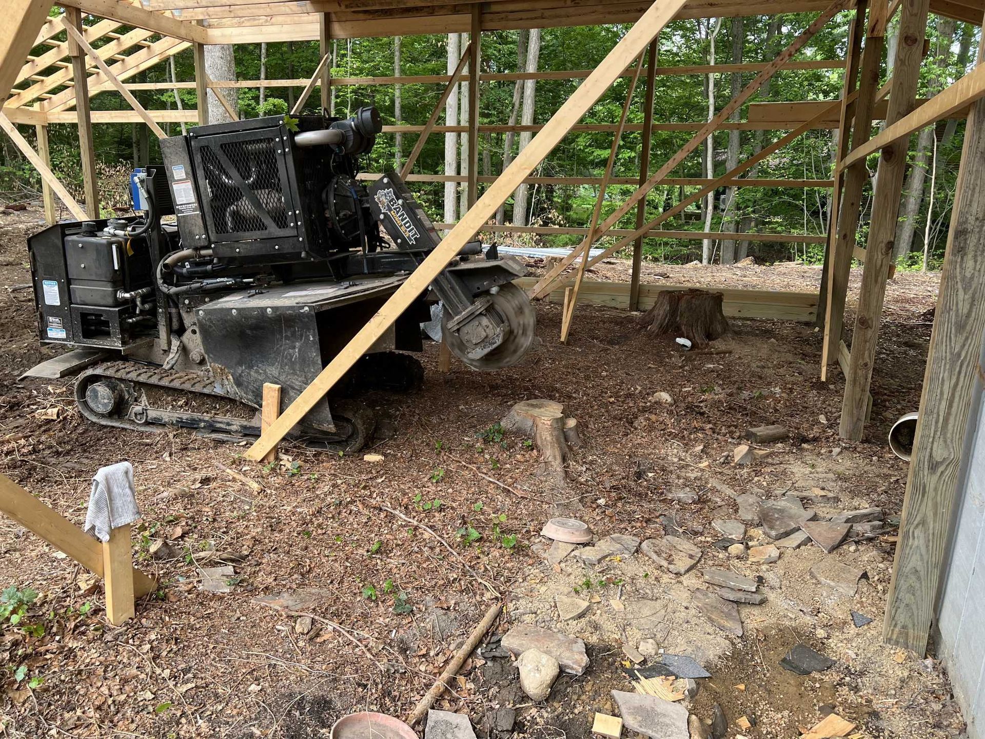A bulldozer is parked under a wooden structure in the woods.