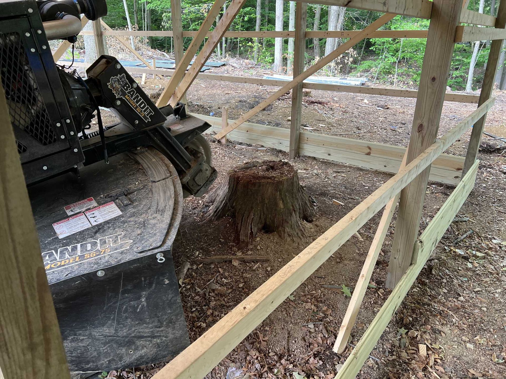 A tree stump is being removed by a machine behind a wooden fence.
