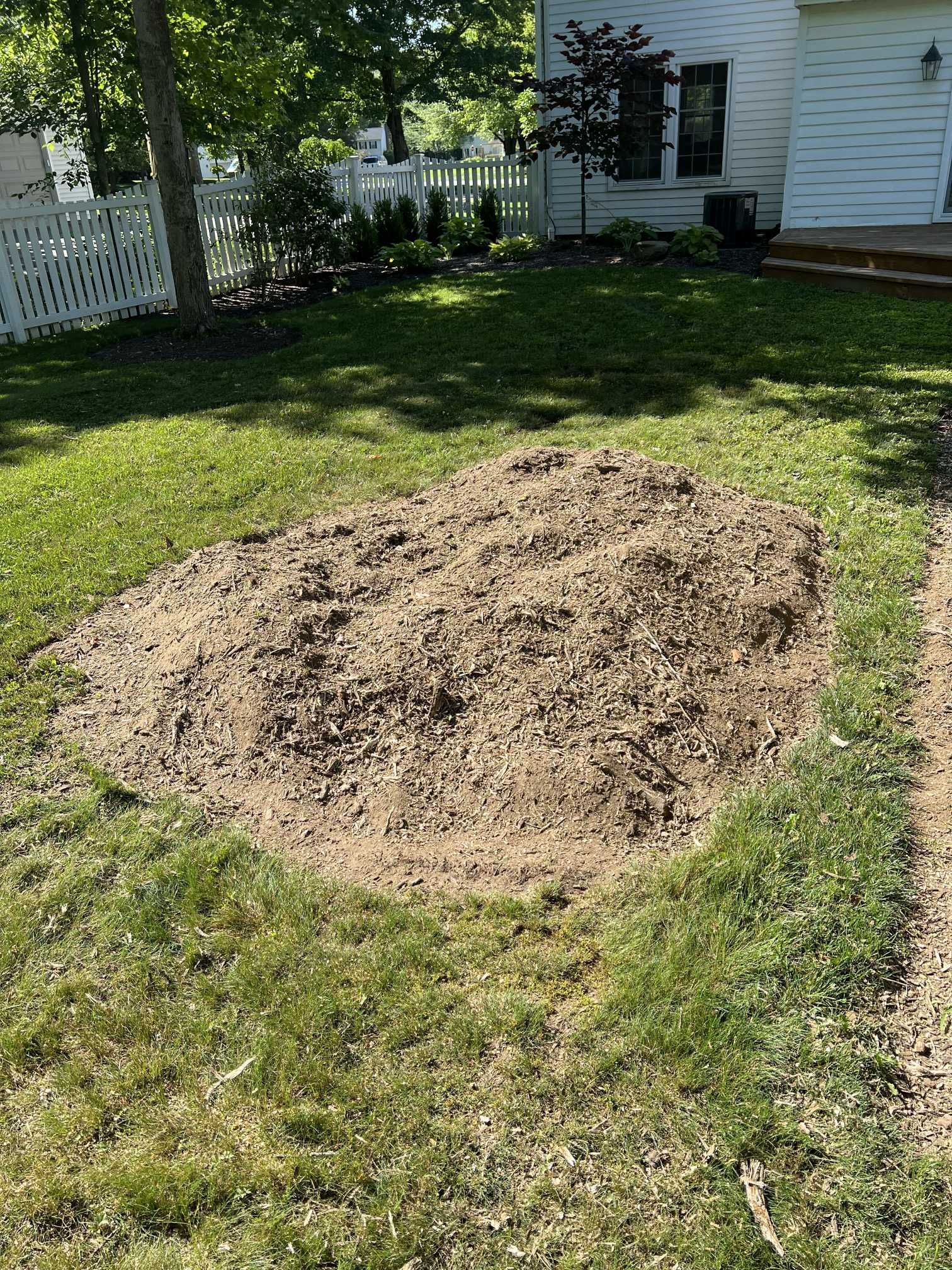 A large pile of dirt is in the middle of a lush green lawn in front of a house.