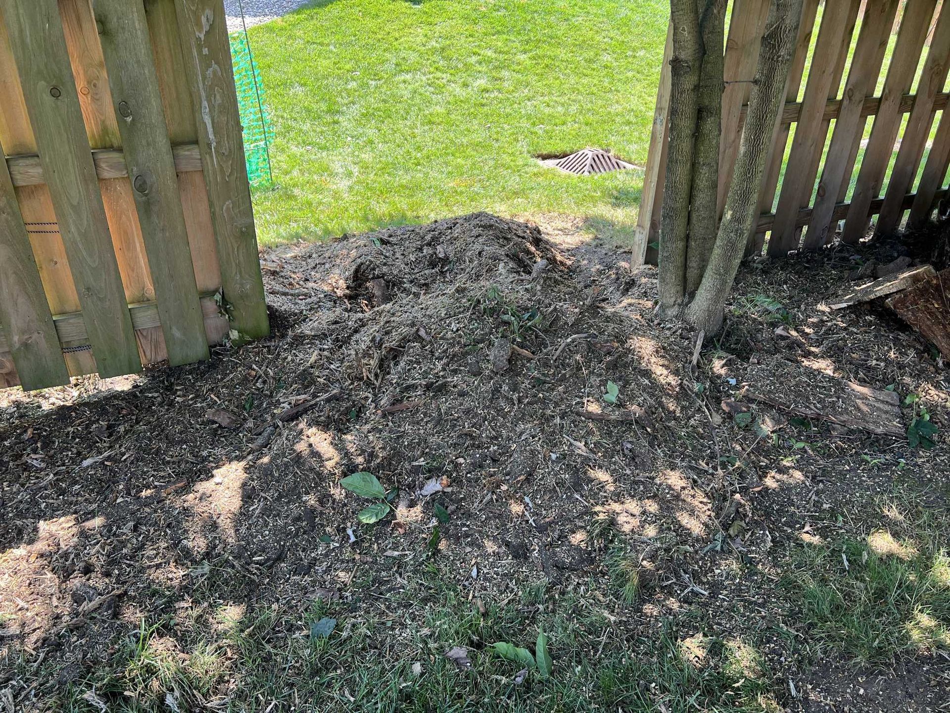 A pile of dirt is sitting in the grass next to a wooden fence.
