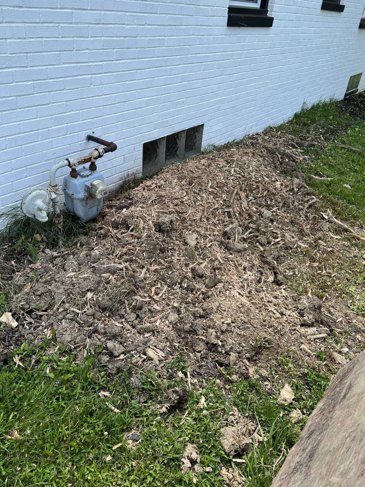 A hose is sitting in the dirt next to a white brick wall.