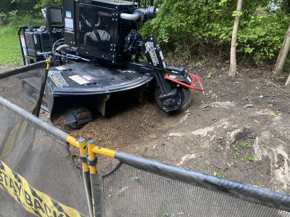 A stump grinder is sitting in the dirt next to a fence.