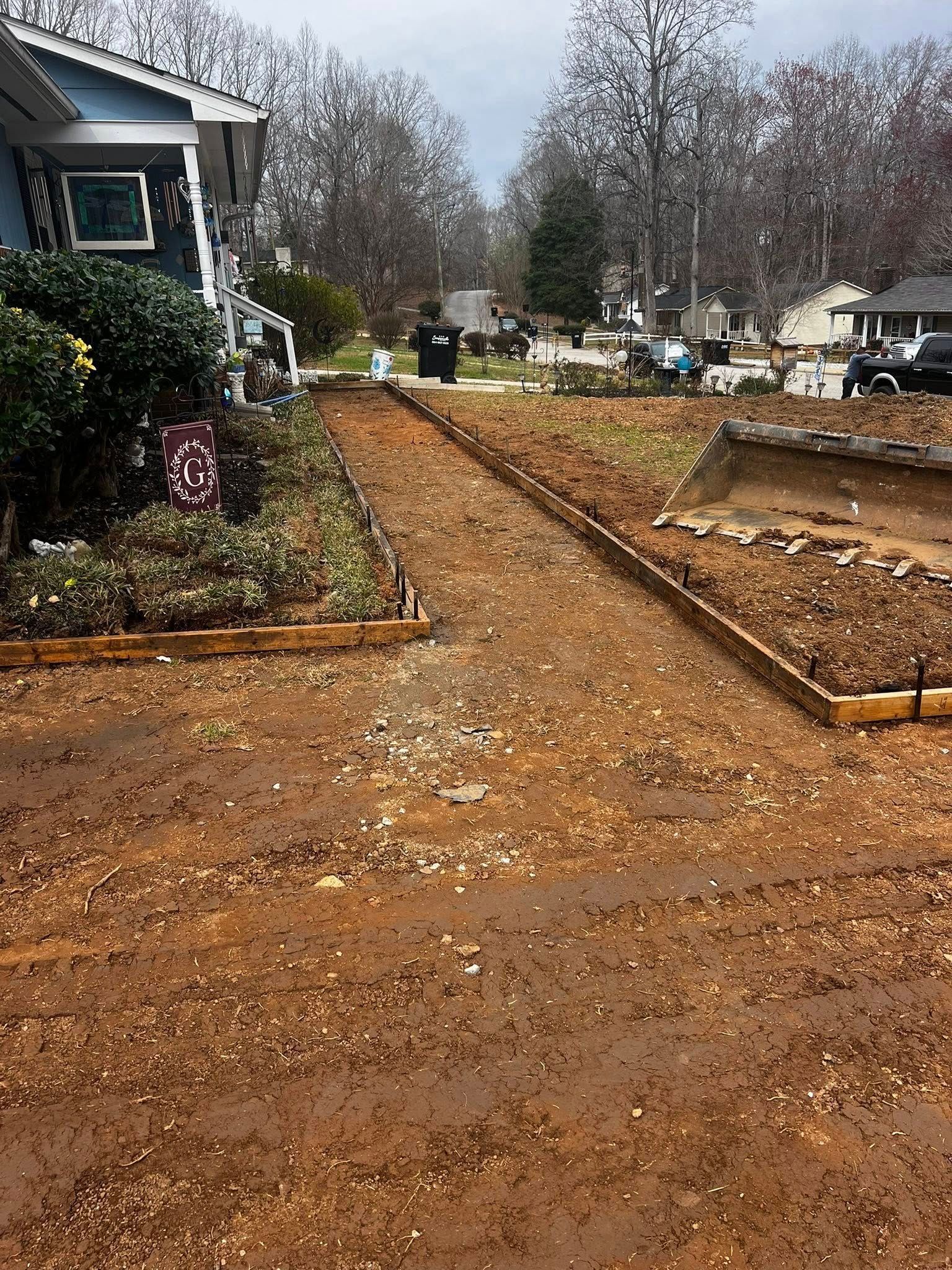 Muddy yard under construction; wood framing defines potential garden beds and walkway. House visible.
