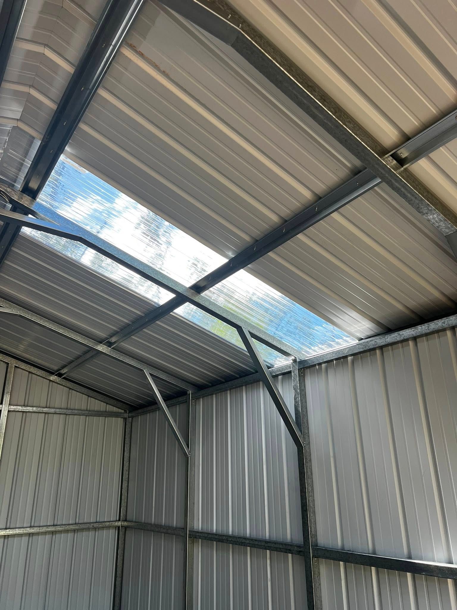 Interior view of a metal shed with a skylight, showing a metal frame and corrugated walls.