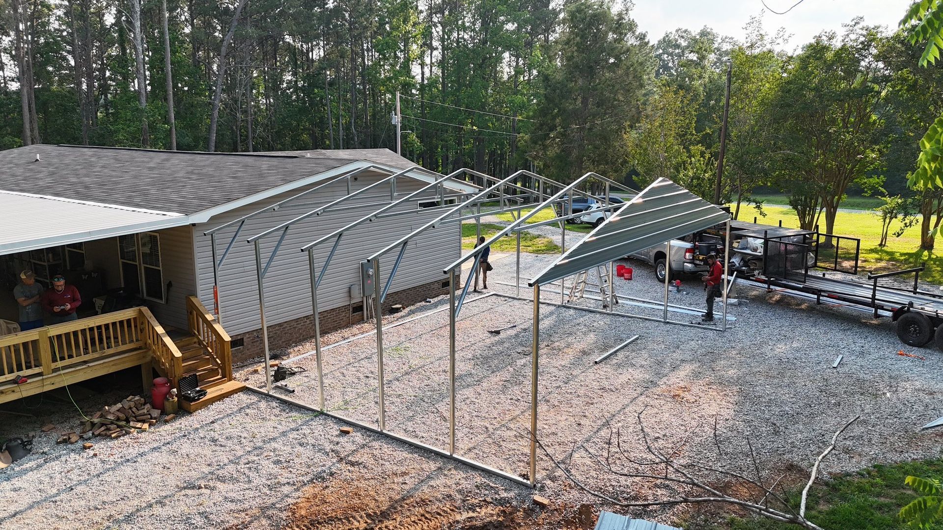 Construction site with a building and a metal frame structure being erected, trees and vehicles present.