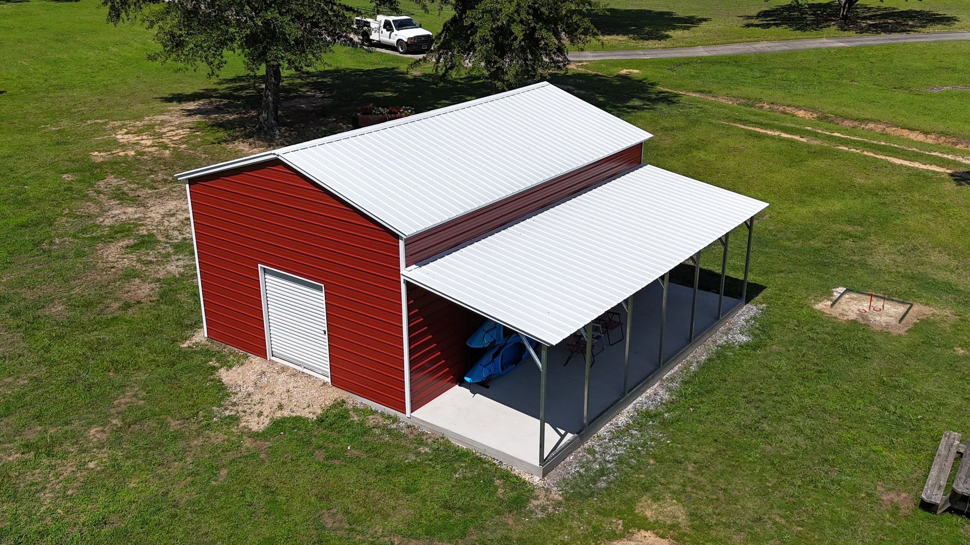 Red barn with white roof and attached awning on green grass.