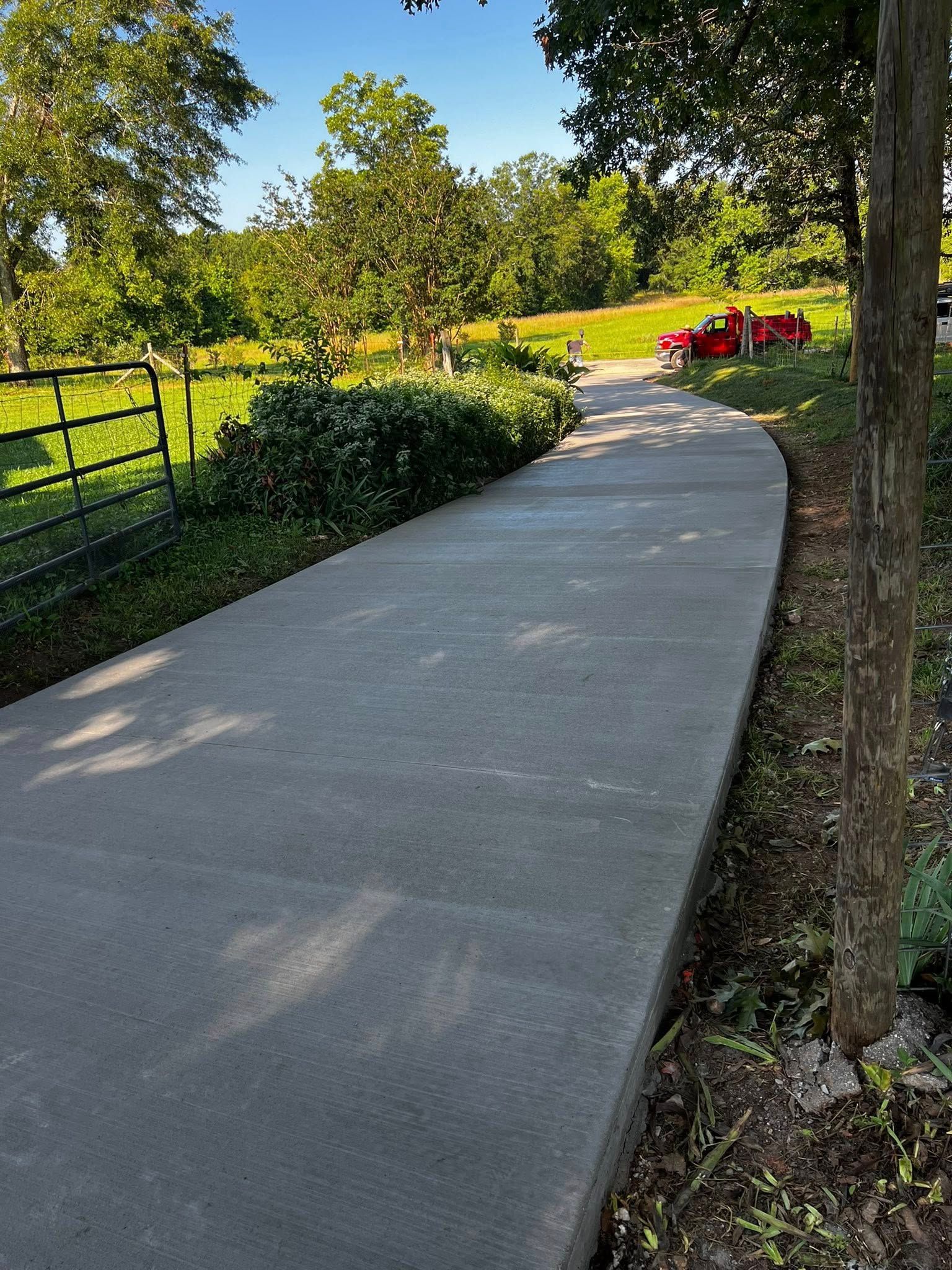 Concrete walkway curving through a green, grassy landscape, a tree to the right.