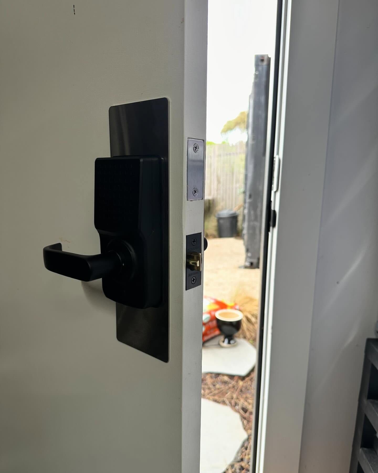 Black Smart Lock on an Open White Door, Showing a Backyard View — Great Ocean Locksmiths in Belmont, VIC