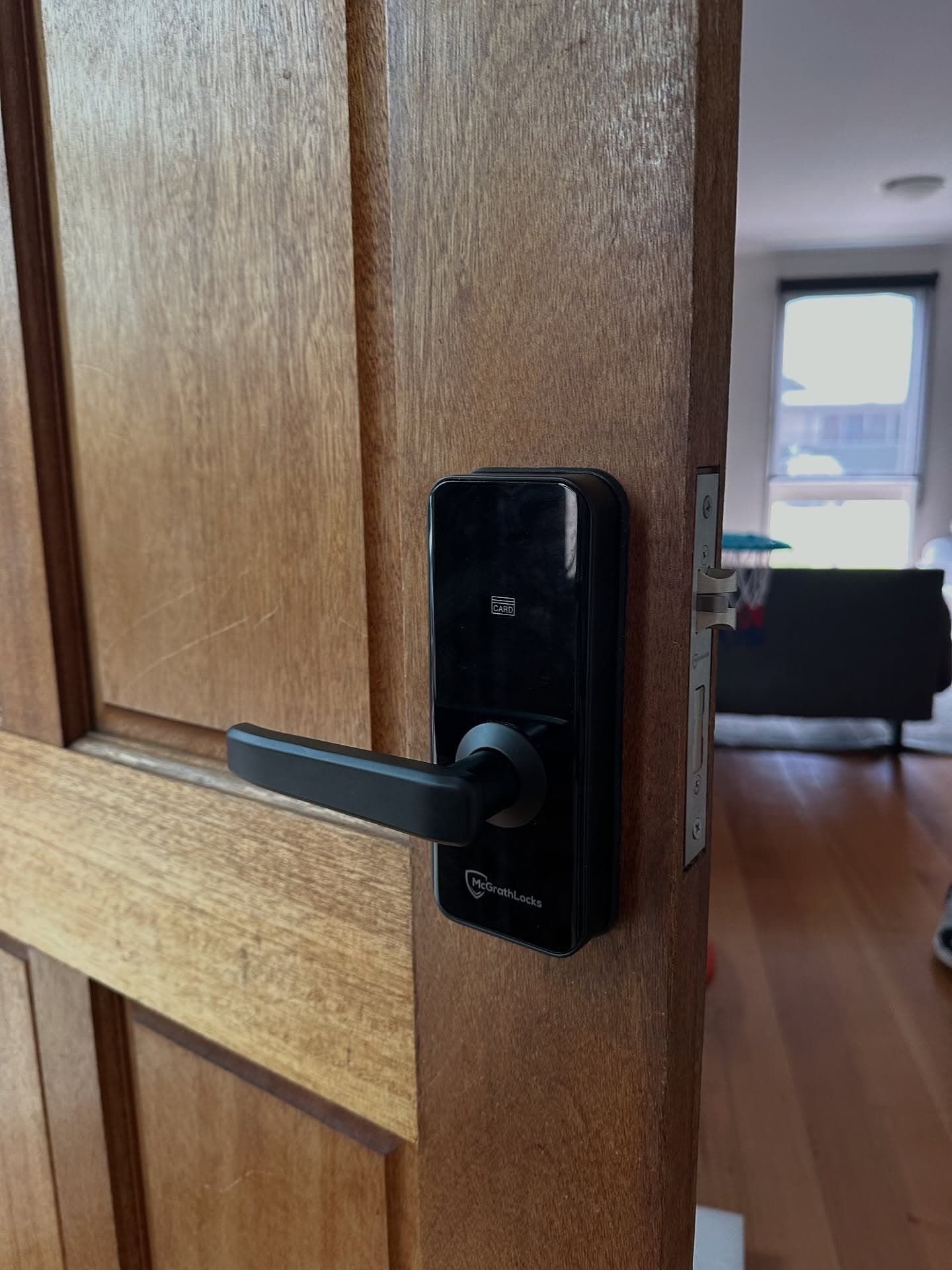 Black Smart Lock With Lever Handle on a Brown Wooden Door, Interior Setting — Great Ocean Locksmiths in Anglesea, VIC