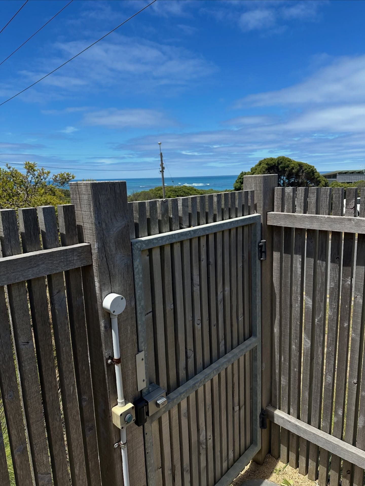 Wooden fence with gate opens to a view of the ocean and blue sky on a sunny day — Great Ocean Locksmiths in Belmont, VIC