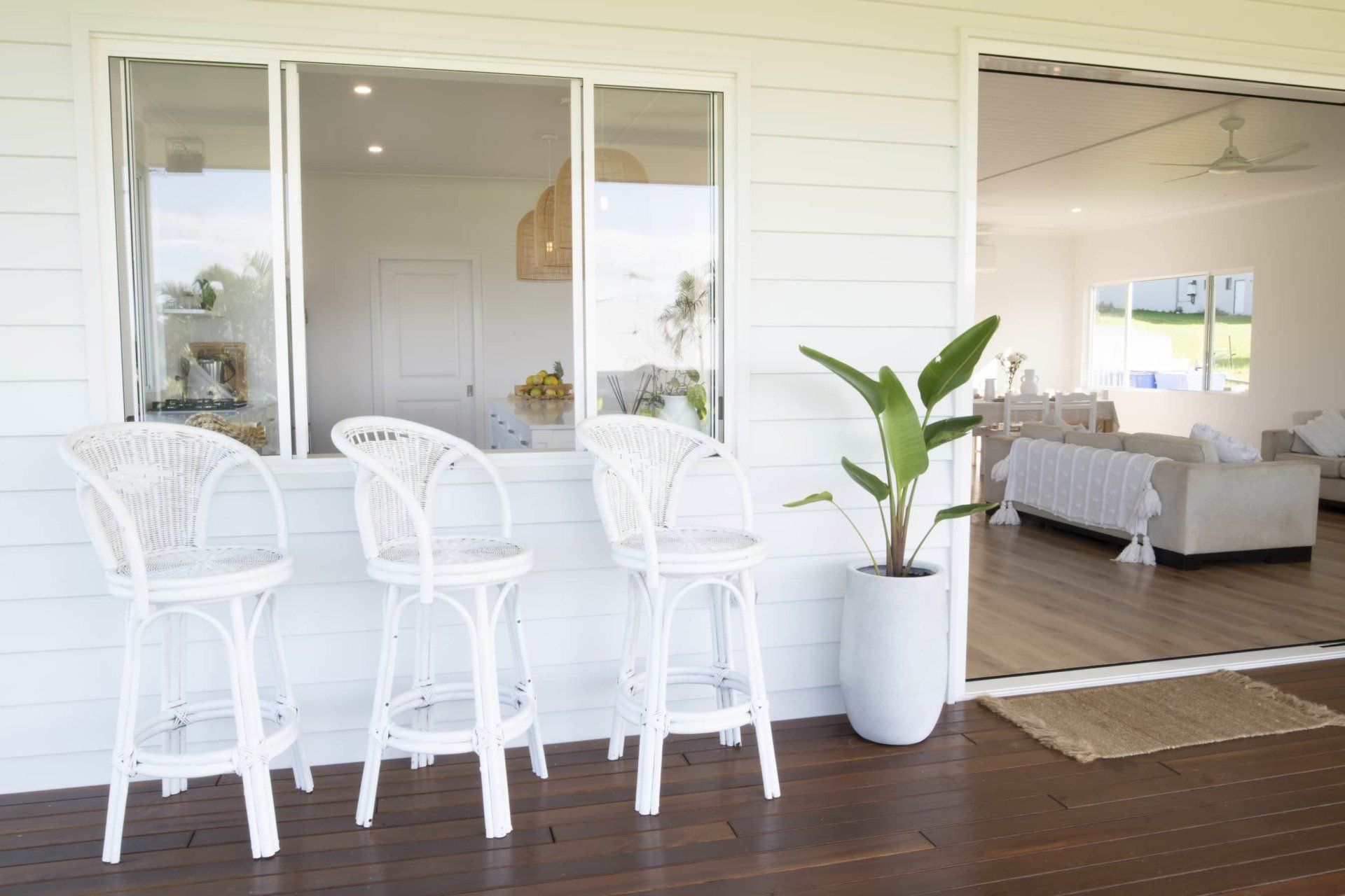 Three white wicker chairs are sitting on a porch next to a window.