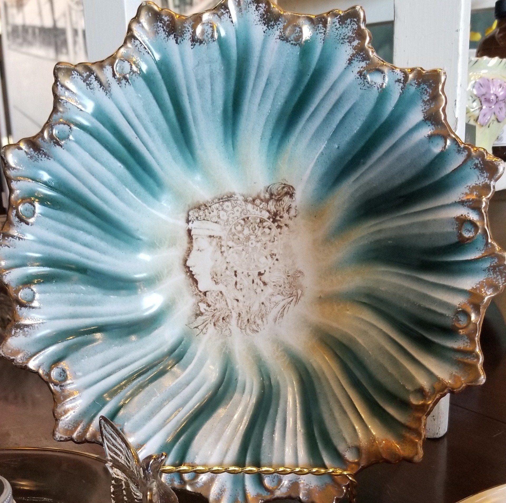 Decorative teal and gold scalloped serving plate on a gold wire stand, featuring a face in the center.