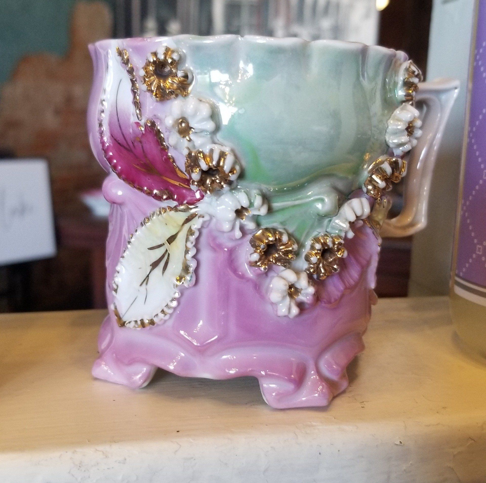 Small, ornate porcelain cup with pink, green, and gold floral accents.
