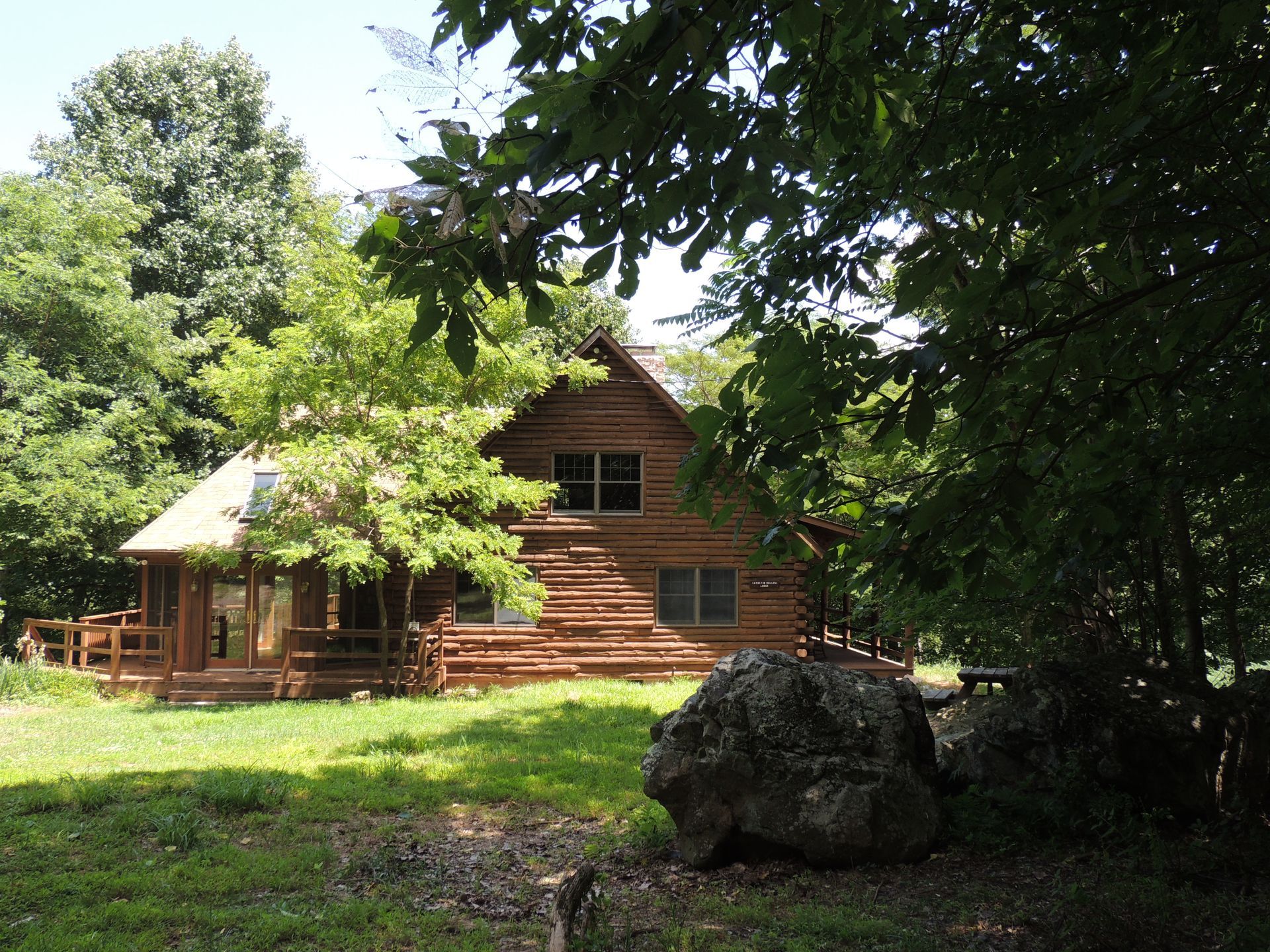 Thr front view of Catoctin Hollow Lodge shows a wooden porch and is surrounded by trees.