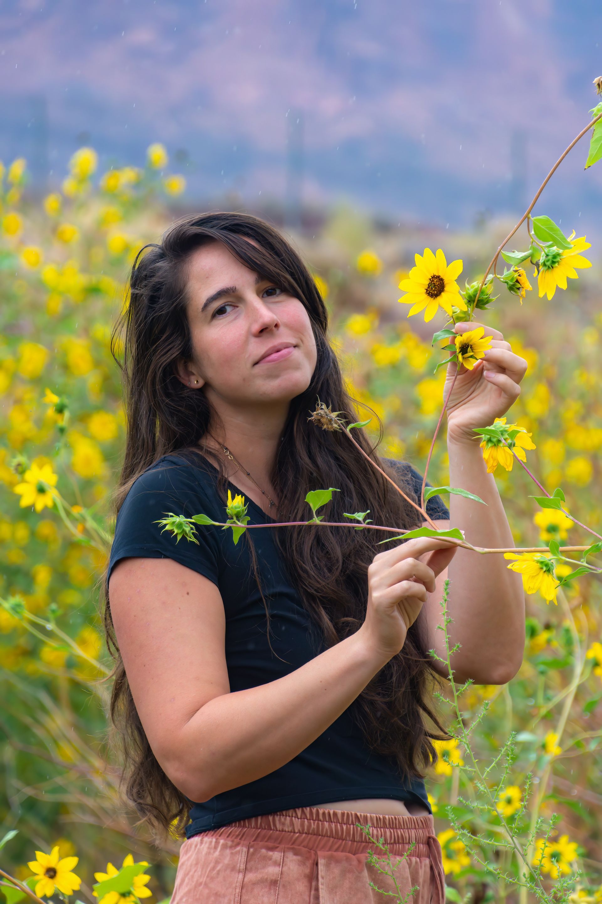 photo of Christine standing in a field of sunflowers, holding a sunflower in one hand.
