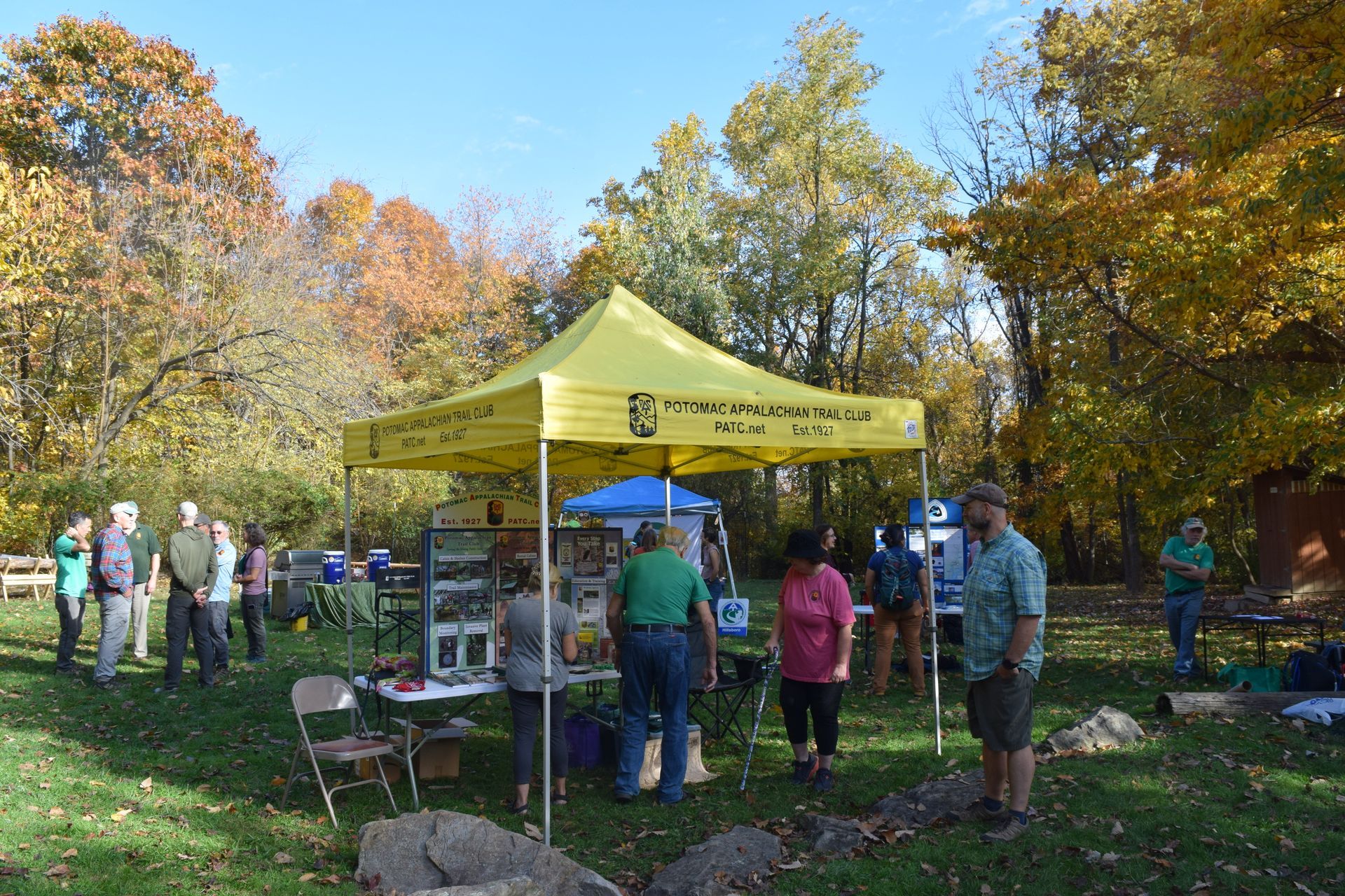 A group of people are standing around a yellow tent in a park.