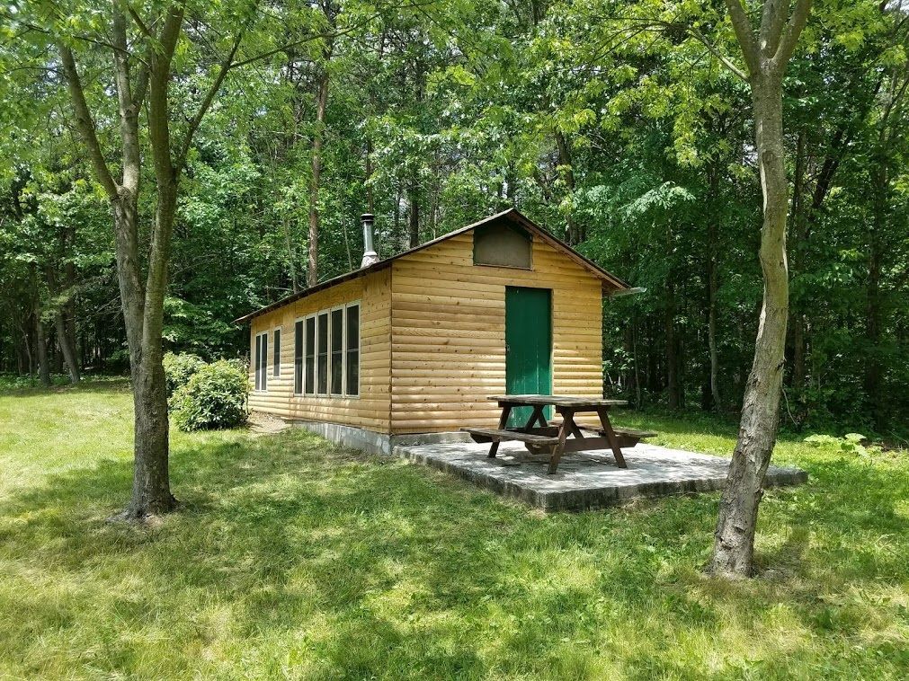 A PATC cabin, The Dawson Cabin featuring a green door and wooden picnic table, situated in the middle of the forest.