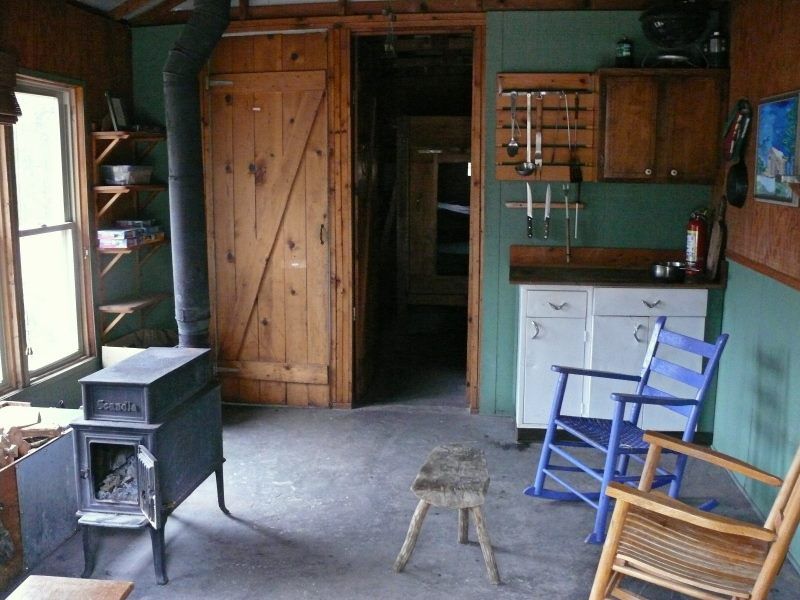 The inside of the Dawson Cabin features wooden rocking chairs, a coal oven, and a wooden kitchen.