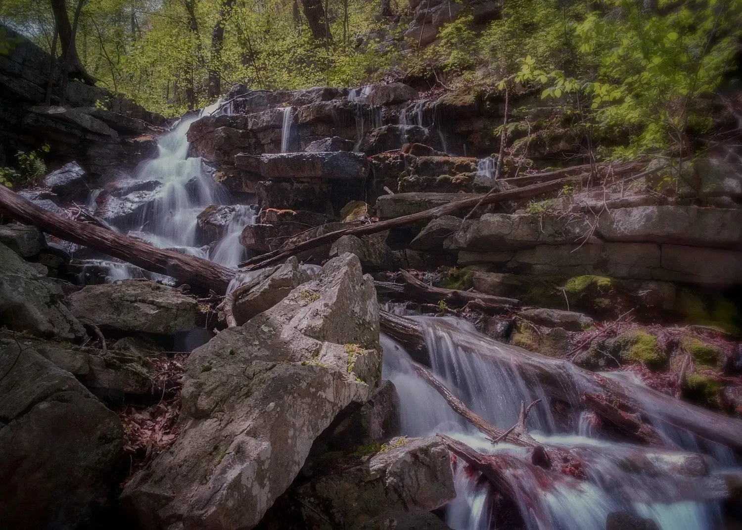 A waterfall is surrounded by rocks and trees in the woods.