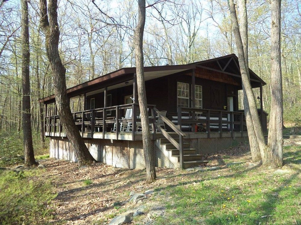 The side view of the Gypsy Spring Shelter features stairs and a wrap-around front porch, featuring wooden chairs and a picnic table.