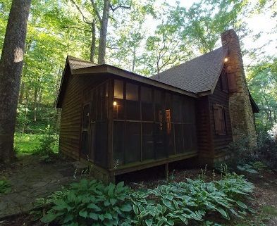 A wooden and stone PATC cabin, with a screen porch, is situated in the middle of the forest.