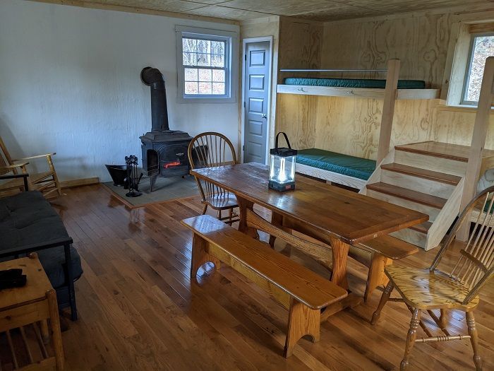 The inside of the cabin features a wooden table and chair, a small fireplace, and a wooden staircase.