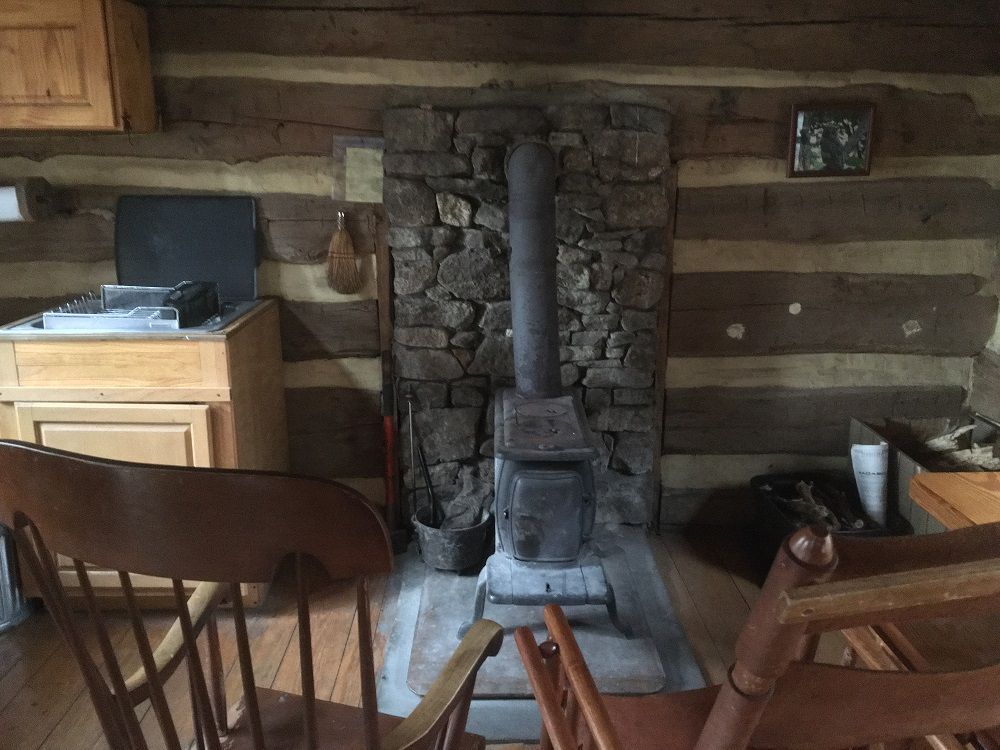 The interior of Johns Rest cabin showing a small kitchen, a small fireplace, and wooden chairs.