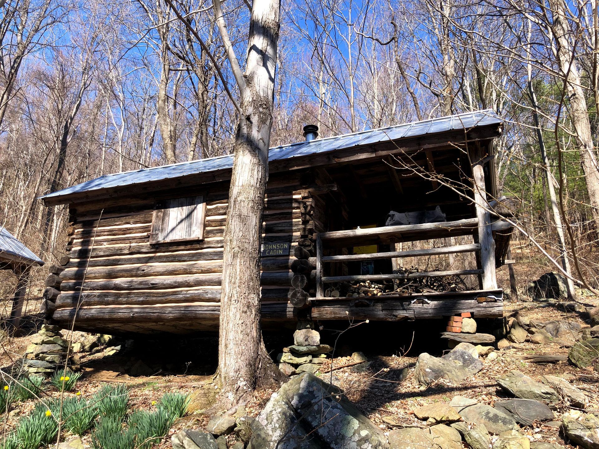 The side view of the Johnson cabin shows a small porch, with surrounding rocks and trees in the area.