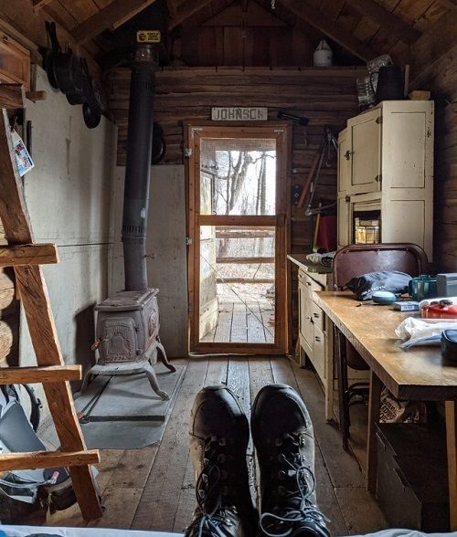 The interior of Johnson cabin shows a small kitchen with a wooden counter, a small fireplace, and cooking area.
