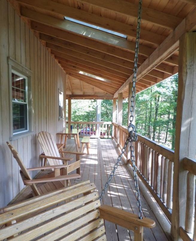 The front porch of the Little Cove Cabin, with wooden chairs and a wooden hanging chair.